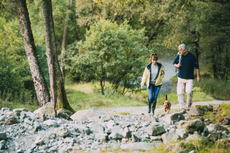 Older couple hiking together on a rocky trail through green woods