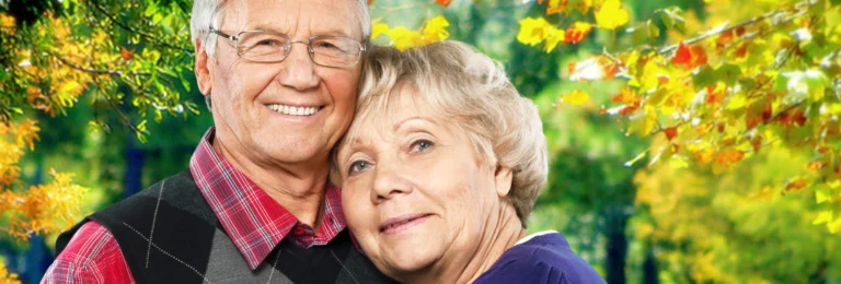 Smiling senior couple embracing in front of autumn leaves