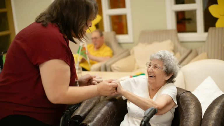 Caregiver holding hands with a smiling senior woman in a living room