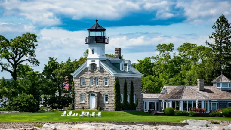 Lighthouse tower on a stone house surrounded by trees under a blue sky