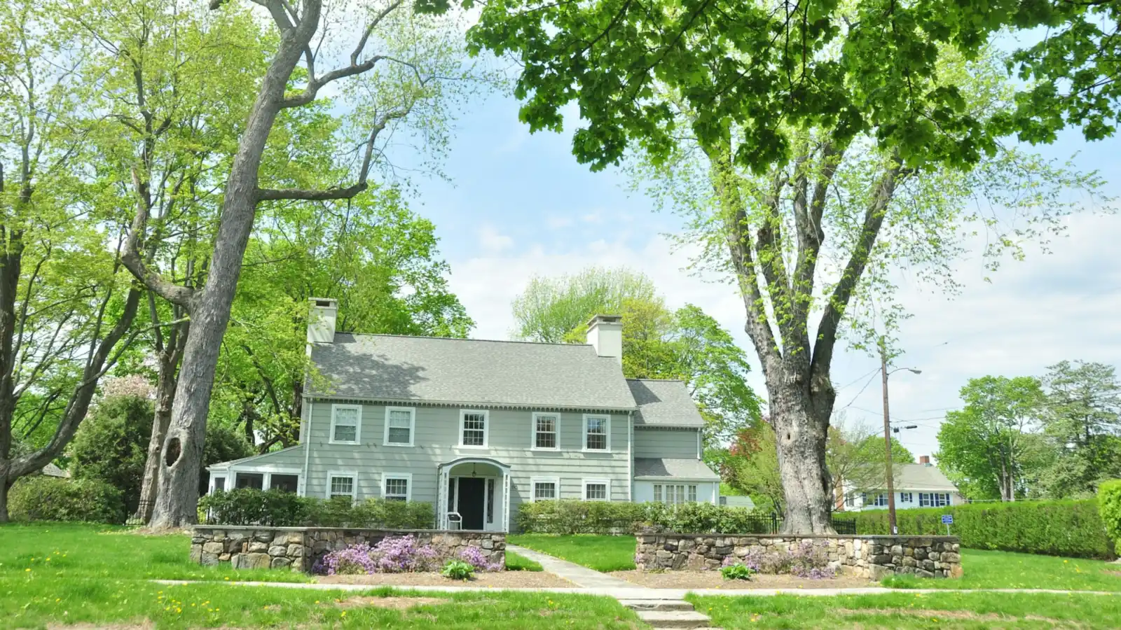 Two-story colonial-style house with a stone wall and a green lawn