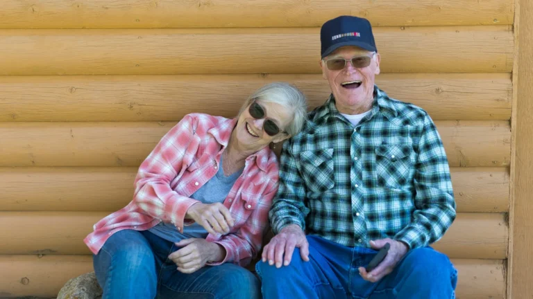 Smiling senior couple sitting together and laughing in front of a log wall