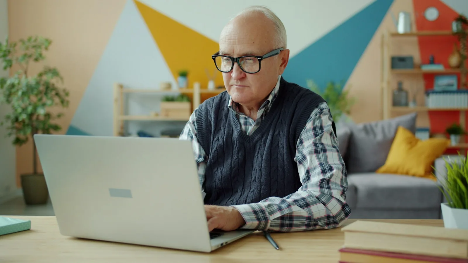Senior man in glasses typing on a laptop at home